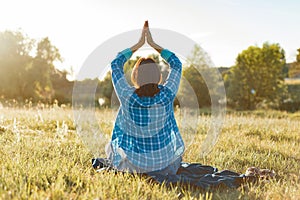 Woman meditating, practicing yoga in nature, view from the back. Sunset, rustic landscapes, green meadow