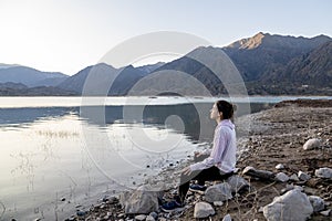 Woman meditating on the shore of a lake while enjoying the nature landscape.