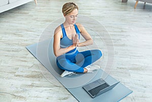 Woman meditating sitting in lotus position on mat with pc