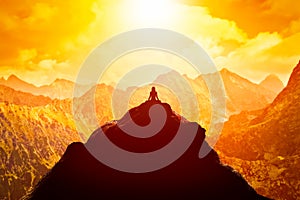 Woman meditating in sitting yoga position on the top of a mountains above clouds at sunset.