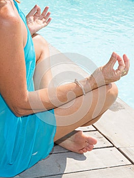 Woman meditating on a wooden deck under tranquil blue water