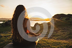 Woman meditating yoga alone at sunrise mountains. View from behind