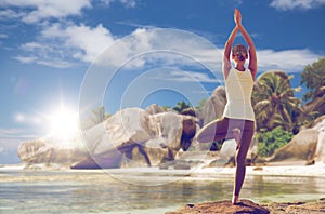 Woman meditating in yoga tree pose over beach