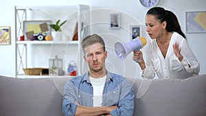 Woman with megaphone shouting on man at home, unsuccessful marriage, conflict