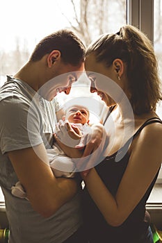 Woman and man holding on hands a newborn. On the background window. Mom, dad and baby. Portrait of young family. Happy family life