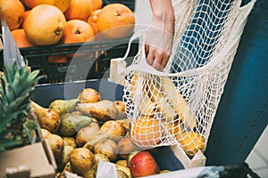 Woman with mesh bag full of fresh vegetables shopping at the store, zero waste concept