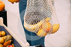 Woman with mesh bag full of fresh vegetables shopping at the store, zero waste concept