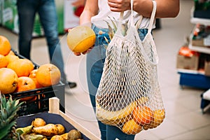 Woman with mesh bag full of fresh vegetables shopping at the store, zero waste concept