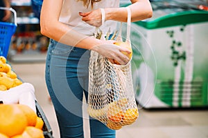 Woman with mesh bag full of fresh vegetables shopping at the store, zero waste concept