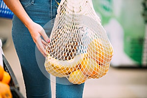 Woman with mesh bag full of fresh vegetables shopping at the store, zero waste concept