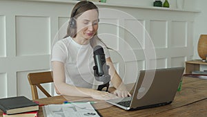 Woman with microphone and laptop computer talking and recording podcast at studio