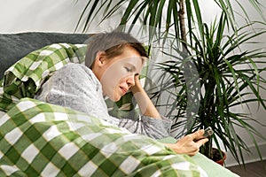 A woman of middle age, sporting a short haircut, stays in bed all day, fixated on her phone. Indolence, apathy, seeking photo