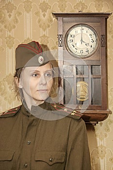 A woman in a military uniform against the background of old paper wallpaper and a clock with a pendulum.