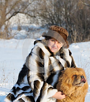 The woman in a mink fur coat plays with a dog