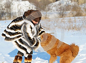 The woman in a mink fur coat plays with a dog