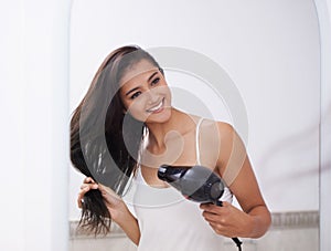 Woman, mirror and blow dryer for haircare and transformation in bathroom, grooming and morning routine. Indian female