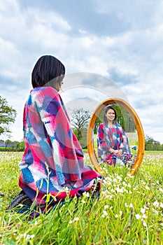 Woman with mirror sitting in blooming meadow