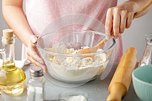 Woman mix flour, baking powder, salt, oil and hot water in the glass bowl.