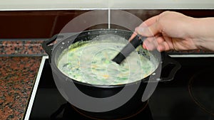 Woman mixes cheese soup in a saucepan on stove