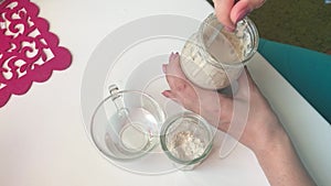 A woman mixes fermented sourdough bread. On the table are the ingredients for feeding bread sourdough. Flour and water.