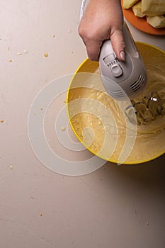 A woman mixes the ingredients for a pie in a yellow bowl with an electric mixer