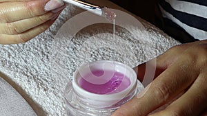 Woman mixes and spreads pink nail polish gel in a small bottle with a brush