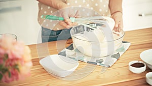 A woman mixing an egg cream with a whisk in a glass bowl.