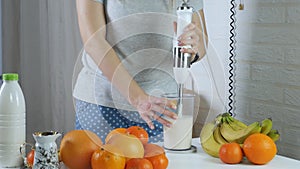 Woman mixing fruit cocktail using blender in kitchen