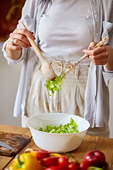 Woman mixing leaf of salad and vegetables ina white bowl