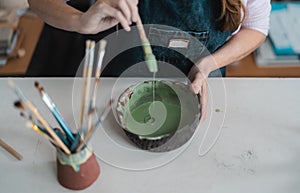 Woman mixing paint with brush inside ceramic bowl in workshop studio