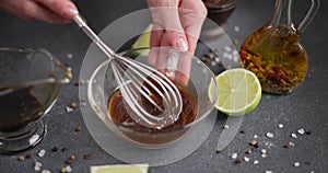 Woman mixing teriyaki say sauce and olive oil with whisk in a glass bowl preparing marinade
