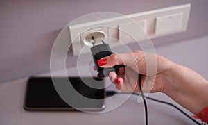 Woman with mobile phone charger in a socket on wall