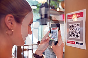 Woman With Mobile Phone Checking Into Venue Scanning QR Code During Health Pandemic