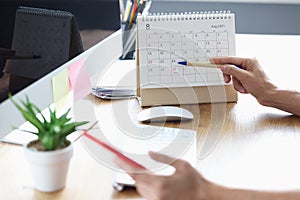 Woman with mobile phone in her hands pointing with pen to date on desk calendar closeup