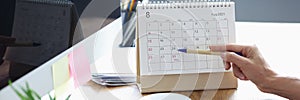 Woman with mobile phone in her hands pointing with pen to date on desk calendar closeup
