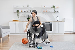 Woman with mobility impairment dribbling ball in studio apartment on weekend.