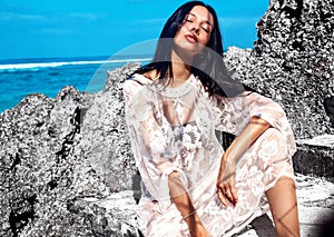 Woman model with dark long hair in transparent white long blouse dress posing near rocks