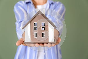 Woman with model of house on color background, closeup. Ecology concept