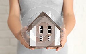 Woman with model of house on light background, closeup. Ecology concept