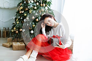 Woman model in a red dress in a photo studio holding a New Year& x27;s gift in her hands
