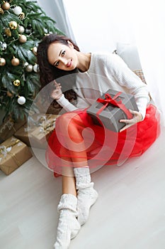 Woman model in a red dress in a photo studio holding a New Year& x27;s gift in her hands