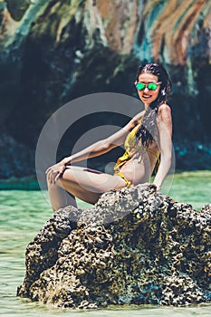 Woman model in a yellow bikini posing on a rock in Maya Bay, Phi Phi Leh, Thailand