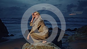 Woman modeling coast rocks at twilight sky. Fashion girl shooting evening beach