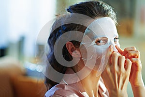 Woman at modern home in sunny winter day applying facial mask