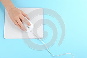 Woman with modern wired optical mouse and pad on blue background, top view. Space for text