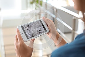 Woman monitoring modern cctv cameras on smartphone indoors