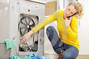 Woman mopping up leaking sink on phone to plumber