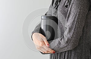 Woman with mortuary urn on light background