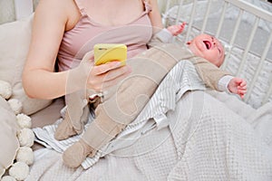 A woman mother breastfeeding a crying infant baby with a phone in her hand. Mom problems with breastfeeding and finding a solution