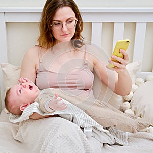 A woman mother breastfeeding a crying infant baby with a phone in her hand. Mom problems with breastfeeding and finding a solution